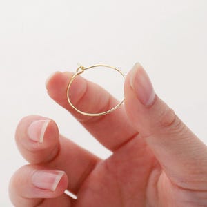 May include: A gold hoop earring, held in a hand, with a simple, circular design.