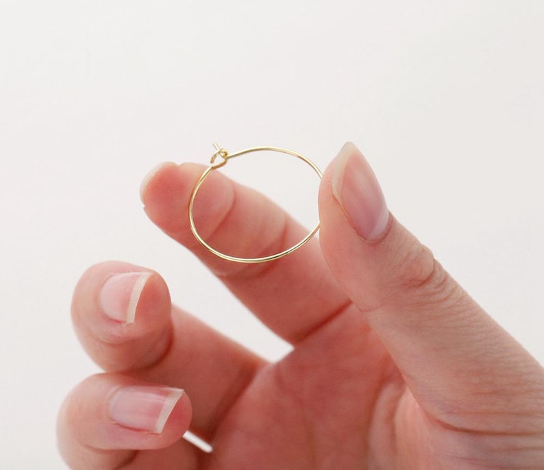 May include: A gold hoop earring, held in a hand, with a simple, circular design.