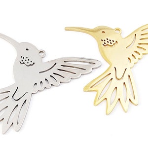 Puede incluir: Dos abalorios de metal en forma de colibrí, uno plateado y otro dorado, con intrincados diseños recortados. Los abalorios son perfectos para la elaboración de joyas o manualidades.
