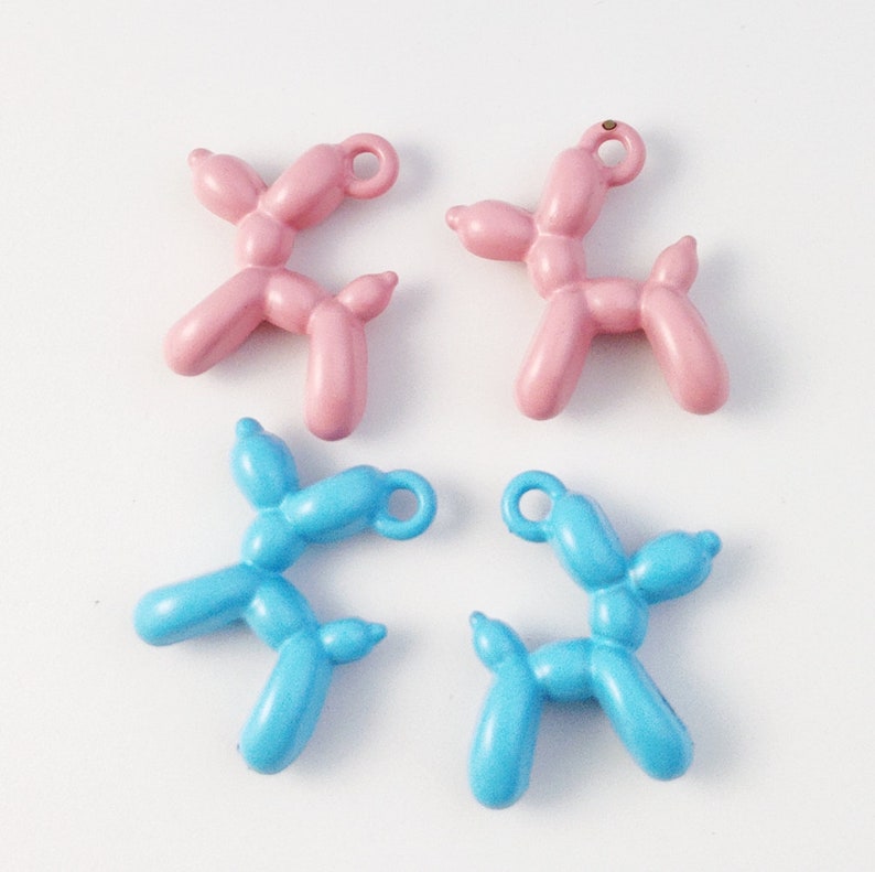 May include: Four balloon animal charms, two pink and two blue, shaped like dogs. The charms have a gold loop for attaching to a necklace or bracelet.