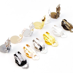 May include: An assortment of clip-on earring findings in silver, gold, and bronze tones. Each finding features a flat, circular pad for attaching earrings and a hinged clip mechanism for securing to the ear.
