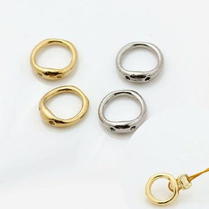 May include: Four small, irregular circular metal rings with two tiny holes on one side, featuring two gold-toned and two silver-toned pieces. An additional gold-toned ring is attached to a thin yellow cord, showing the functional use of the items.