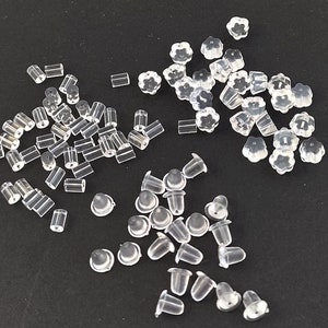 Può includere: Assortimento di chiusure per orecchini in plastica trasparente di varie forme e dimensioni. Le chiusure includono piccoli cilindri, piccole forme di fiori e piccole cupole.