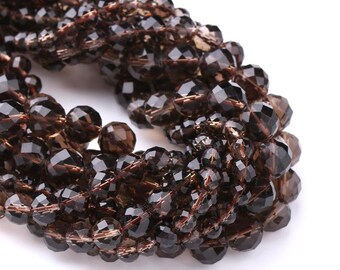 May include: Strand of faceted, smoky quartz beads. The beads are a deep brown color with a faceted cut, creating a sparkling effect. The beads are strung together, forming a necklace or bracelet.