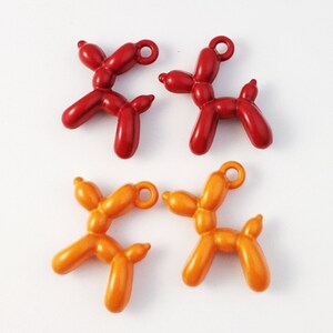 May include: Four balloon animal charms, two red and two orange. The charms are shaped like dogs and have a loop at the top for attaching to a necklace or bracelet.