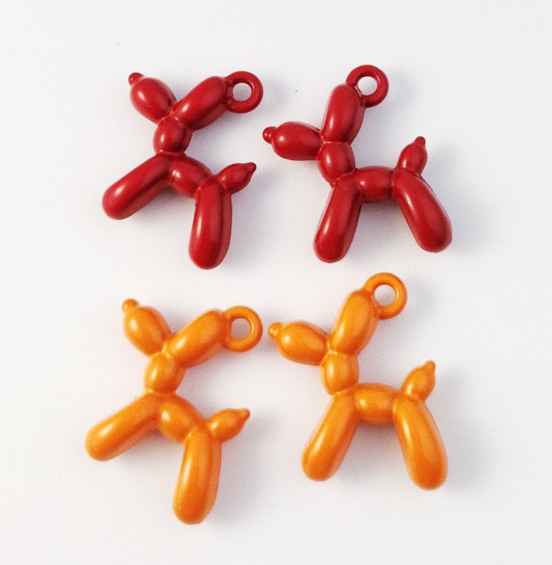 May include: Four balloon animal charms, two red and two orange. The charms are shaped like dogs and have a loop at the top for attaching to a necklace or bracelet.