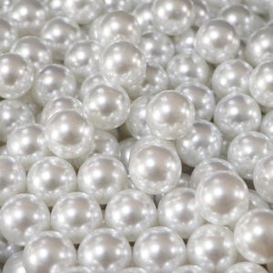 May include: A close-up shot of numerous white, round pearls. The pearls have a lustrous, reflective surface, and are tightly packed together, filling the frame. The pearls are a creamy white color, and the lighting creates highlights and shadows.