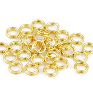 Może przedstawiać: Stosik złotych kółek do łączenia, rodzaj elementu biżuteryjnego używanego do łączenia łańcuszków, sznurków i innych elementów biżuterii.