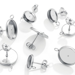 May include: Six silver-toned earring settings with a round or oval-shaped bezel for adding a cabochon. Each setting has a post and a loop for attaching a charm or pendant.
