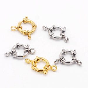 Op de afbeelding: Vier zilveren en gouden metalen sluitingen voor het maken van sieraden. De sluitingen zijn rond met een gedraaid ontwerp en hebben drie lussen om aan een ketting of koord te bevestigen.