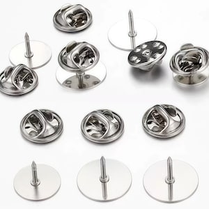 May include: A collection of silver-colored pin backs and clutch fasteners. The image shows various styles, including butterfly clutches, pin backs with flat discs, and a multi-hole clutch. These components are commonly used for attaching pins, badges, and other accessories.