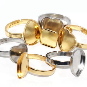 Puede incluir: Un conjunto de anillos ajustables con biseles de diversas formas. Los anillos son dorados y plateados, con formas de lágrima, corazón y cuadradas. Los biseles están diseñados para sujetar piedras u otros elementos decorativos.