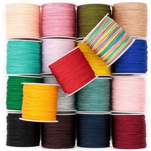 May include: A collection of spools of colorful cord in various shades, including pink, green, blue, yellow, and red. The cords are neatly wound on spools, creating a visually appealing display. The image showcases a variety of colors and textures, perfect for crafting projects.