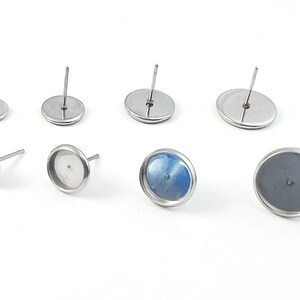 May include: A set of six silver earring settings with a round bezel. The settings are designed to hold a variety of cabochons, including glass, stone, and resin. The settings are made of stainless steel and have a polished finish.