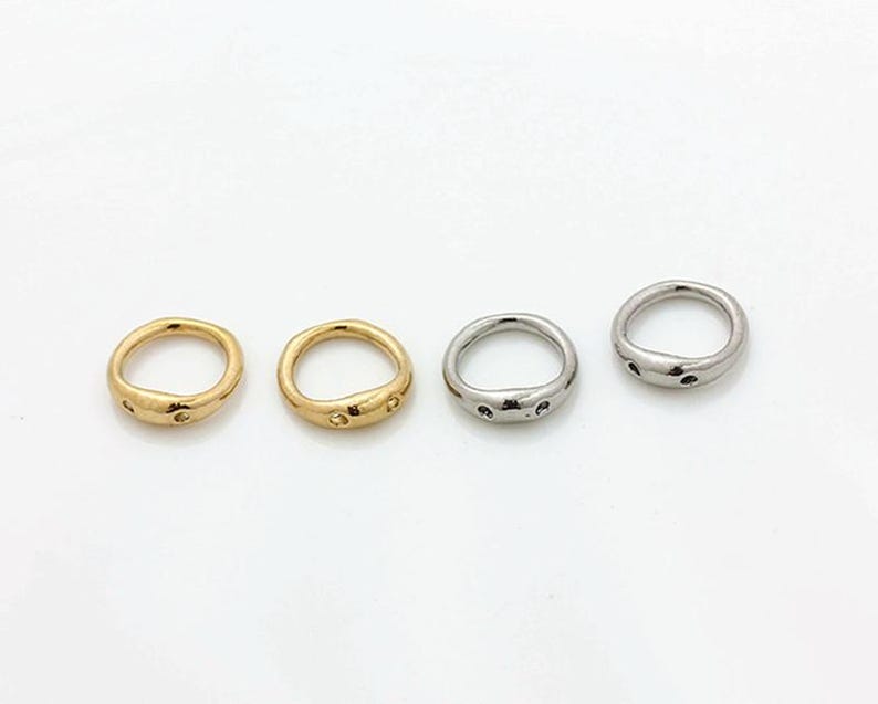 May include: Four rings arranged in a horizontal row. Two rings are gold-toned and two are silver-toned. Each ring features an irregular, organic shape with a smooth, polished surface and two small, circular indentations on the front side.