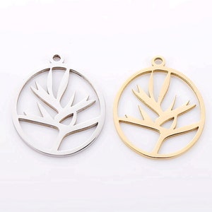 Puede incluir: Dos abalorios de metal en forma de círculo con un diseño de flor de ave del paraíso. El abalorio de la izquierda es plateado y el abalorio de la derecha es dorado.