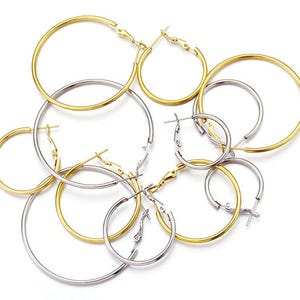 Puede incluir: Un conjunto de seis pendientes de aro en tonos dorados y plateados. Los pendientes son de diferentes tamaños y están dispuestos en un racimo.