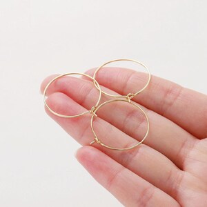 May include: Three gold hoop earrings of different sizes, displayed on a hand.