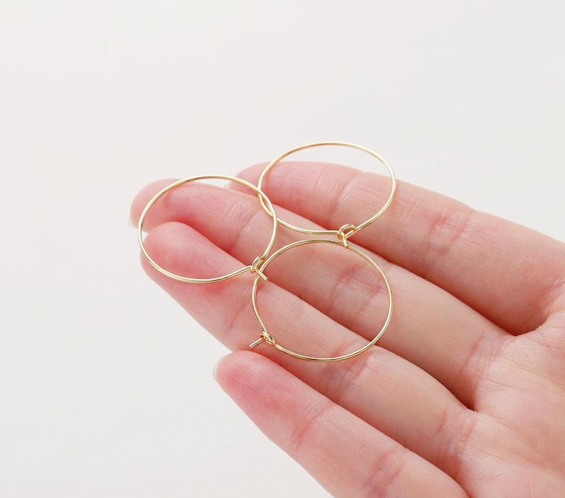 May include: Three gold hoop earrings of different sizes, displayed on a hand.