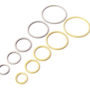May include: A set of nine jump rings in two different sizes and colours. The jump rings are silver and gold, and they are arranged in a descending size order from left to right.