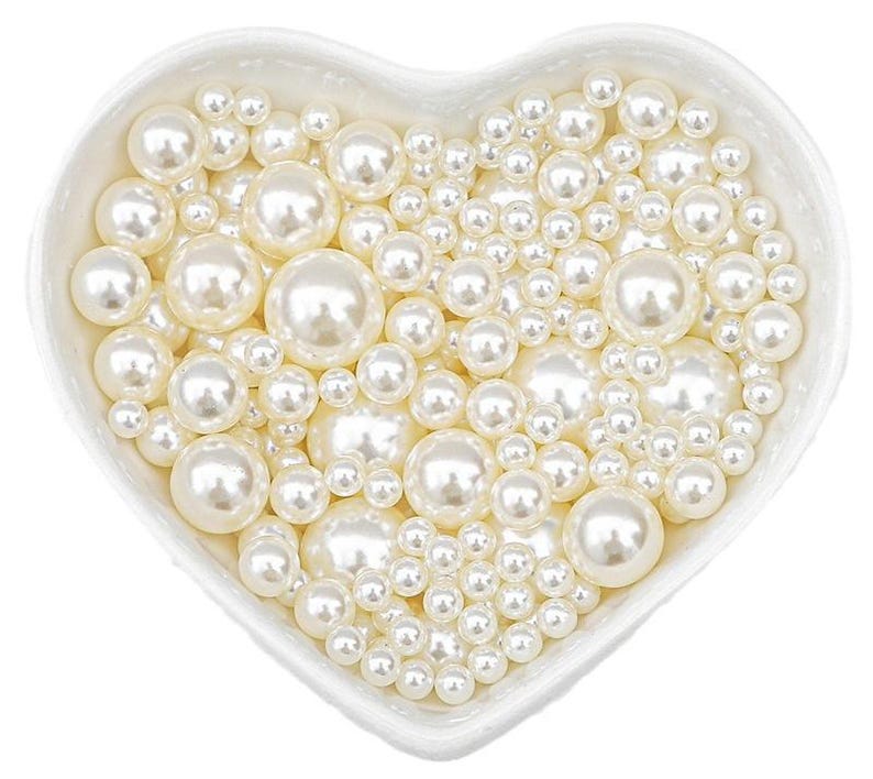 May include: A heart-shaped white ceramic dish filled with various sizes of creamy white faux pearls. The pearls have a lustrous sheen, creating a classic and elegant aesthetic. Ideal for jewelry making or craft projects.