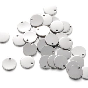 Op de afbeelding: Een stapel ronde zilveren metalen hanger met een klein gaatje in elk. De hangers zijn perfect voor het maken van sieraden, scrapbooking en andere knutselwerkjes.