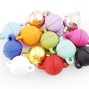 Pode incluir: Uma coleção de fechos magnéticos esféricos coloridos em várias tonalidades, incluindo azul, laranja, verde, rosa e dourado. Cada fecho tem um pequeno laço e uma forma arredondada, ideal para fazer joias ou projetos de artesanato.