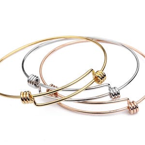 May include: Four bangle bracelets in gold, silver, and rose gold tones. Each bracelet features a coiled design at the clasp. The bracelets are displayed on a white background.