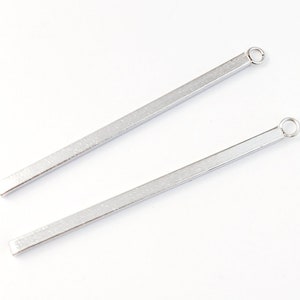 May include: Two silver metal bars with a small loop at the end. The bars are smooth and have a slightly textured surface.