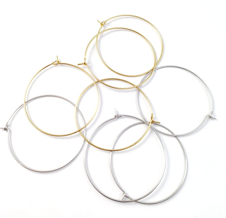 May include: A set of four hoop earrings, two gold and two silver. The hoops are all different sizes and are arranged in a pile.