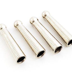 May include: Four silver metal cord ends with a rounded tip. The cord ends have a ribbed texture.