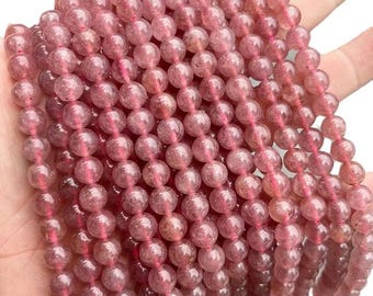 Könnte beinhalten: Stränge aus rosa Edelsteinperlen. Die Perlen sind rund und durchscheinend, mit Farbvariationen. Die Perlen sind aufgefädelt und bilden eine strukturierte Oberfläche. Die Gesamtfarbe ist ein weiches, staubiges Rosa.