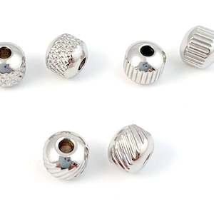 以下が含まれることがあります： 中央に穴が開いた、テクスチャ加工された表面を持つ銀色の金属ビーズ6個。ビーズは丸く、光沢のある仕上げになっています。