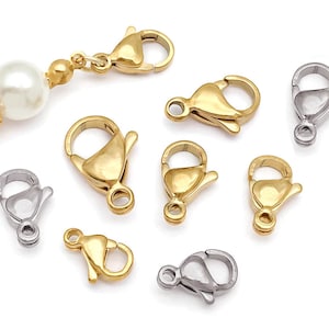 May include: A collection of gold-toned and silver-toned lobster claw clasps in various sizes, featuring a spring-loaded mechanism. One gold-toned clasp is attached to a strand of white spherical beads with small gold-toned spacer beads.