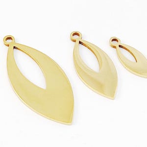 Peut inclure: Trois breloques en métal de forme de feuille dorées avec une découpe au centre. Les breloques ont un trou en haut pour les attacher à des bijoux.