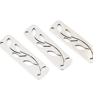 May include: Three silver metal rectangular charms with a cut-out design of a leafy branch.