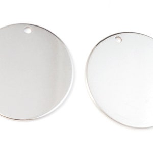 Op de afbeelding: Twee ronde zilveren metalen blanks met een gat aan de bovenkant om op te hangen.