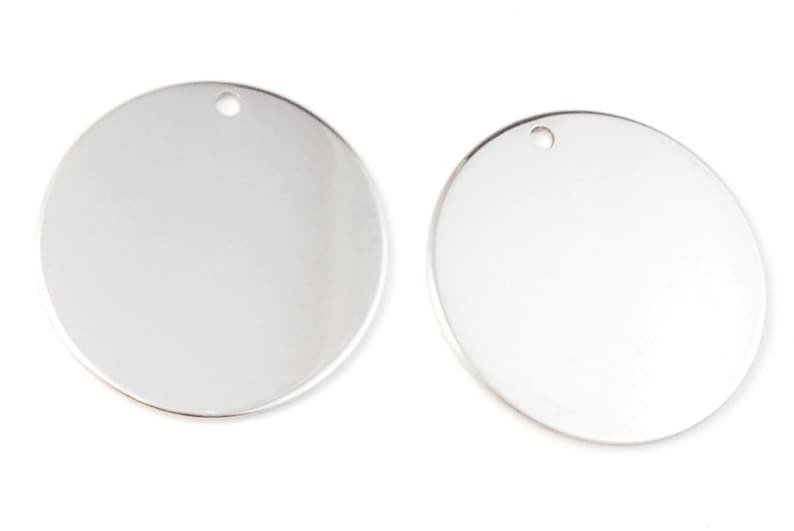 Op de afbeelding: Twee ronde zilveren metalen blanks met een gat aan de bovenkant om op te hangen.