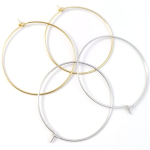 May include: Three hoop earrings, one gold and two silver, are arranged on a white background. The hoops are all the same size and have a simple, elegant design.
