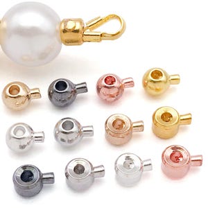 Könnte beinhalten: Eine Sammlung kleiner Schmuckschlaufen aus Metall in verschiedenen metallischen Ausführungen wie Gold, Silber, Roségold und Gunmetal. Jede Schlaufe hat ein kreisförmiges Oberteil mit einem Loch und eine kleine Öse zum Befestigen.