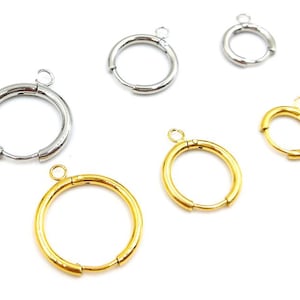 May include: An assortment of hoop earrings in silver and gold tones. The earrings vary in size, with a hinged clasp and a small loop at the top for attaching to a hook. The earrings are displayed against a white background.
