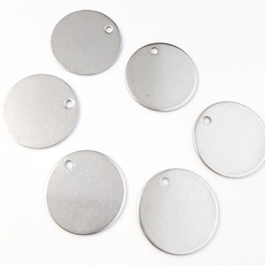 Op de afbeelding: Zes ronde zilveren metalen labels met een gat aan de bovenkant. De labels zijn blanco en klaar om te personaliseren.