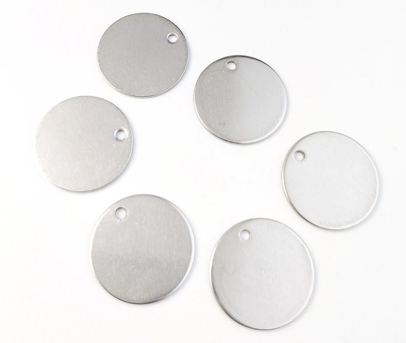 Op de afbeelding: Zes ronde zilveren metalen labels met een gat aan de bovenkant. De labels zijn blanco en klaar om te personaliseren.