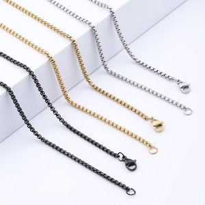 Può includere: Quattro collane a catena diverse in nero, oro e argento. Le catene sono tutte dello stesso stile, una catena a maglie quadrate, ma di colori diversi. Le catene sono tutte su una superficie bianca.