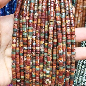 Può includere: Fili di piccole perline quadrate nei toni del marrone, rosso, verde e giallo. Le perline sono tenute in una mano, mostrando le loro tonalità terrose e le variazioni naturali. Ideali per la creazione di gioielli.