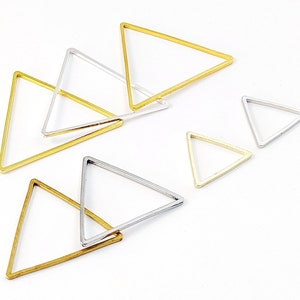 May include: A set of six triangle-shaped metal hoops in gold and silver. The hoops are of varying sizes and are arranged on a white surface.