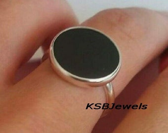 Puede incluir: Un anillo de plata con una piedra ovalada negra. El anillo está en un dedo.