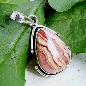 May include: A silver pendant with a teardrop-shaped, pink, white, and brown agate stone. The stone has a swirling pattern.