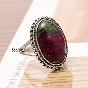Peut inclure: Une bague en argent avec une pierre ovale verte et rose sertie dans une bélière en argent. La bague a un motif de corde autour de la bélière.