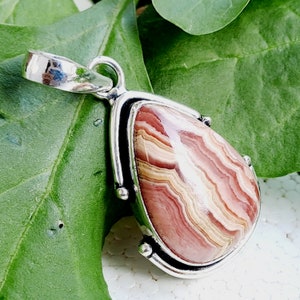 May include: A silver pendant with a teardrop-shaped pink and white agate stone. The stone has a layered, striped pattern.